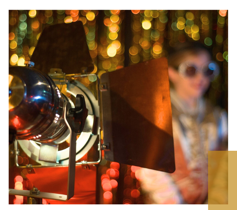 Scheinwerfer mit schwarzem Flügel vor einem Mädchen, bunte unscharfe Lichter im Hintergrund.