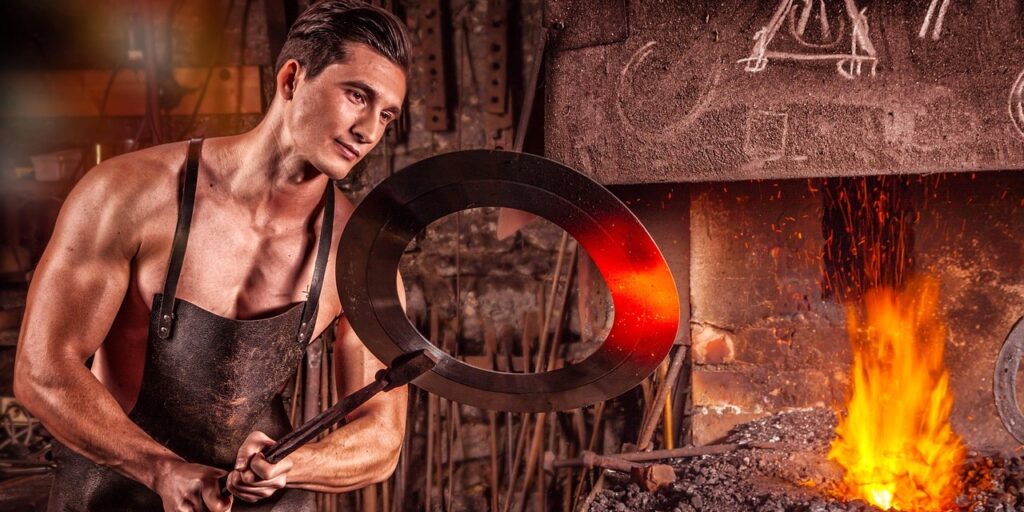 A muscular man wearing a black apron holds a large metal ring near bright orange forge flames, representing skilled craftsmanship and the role of innovation and resilient industrial processes.