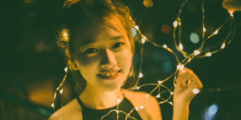 Ein Mädchen hält leuchtende Lichterketten in den Händen in einer dunklen Umgebung – ein Symbol für den Zugang zu sauberer, bezahlbarer Elektrizität, die Leben erhellt und Gemeinschaften stärkt.