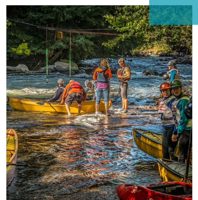 Mehrere Personen stehen und knien am Ufer eines Flusses mit zwei gelben Kanus, umgeben von Bäumen und Felsen. Förderung eines verantwortungsvollen Umgangs mit Gewässer. Nachhaltige Freizeitaktivitäten stärken das Bewusstsein für Gewässerschutz und saubere Wasserwege.