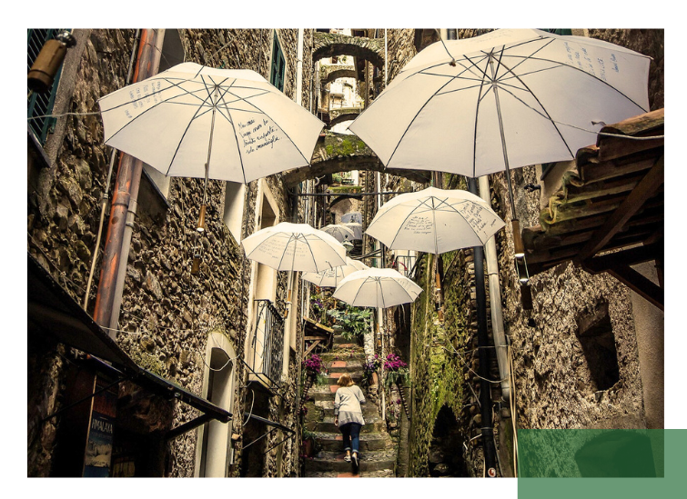 Eine enge steinerne Altstadtgasse mit Treppenstufen ist mit hängenden weißen Regenschirmen dekoriert. Eine Person geht die Stufen hinauf. Die Szene steht für kreative, lebenswerte Stadtgestaltung und den Schutz historischer Stadtstrukturen.