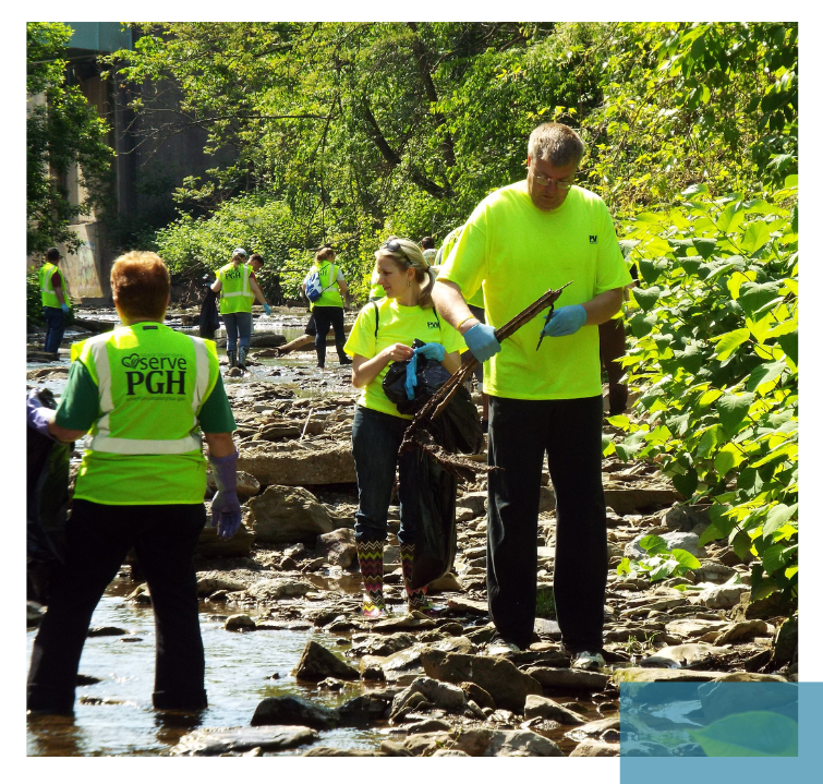 Mehrere Personen in neongelben T-Shirts und Handschuhen sammeln Müll an einem felsigen Bachlauf, umgeben von grünem Laub. Direkter Beitrag zur Reduktion von Verschmutzung.