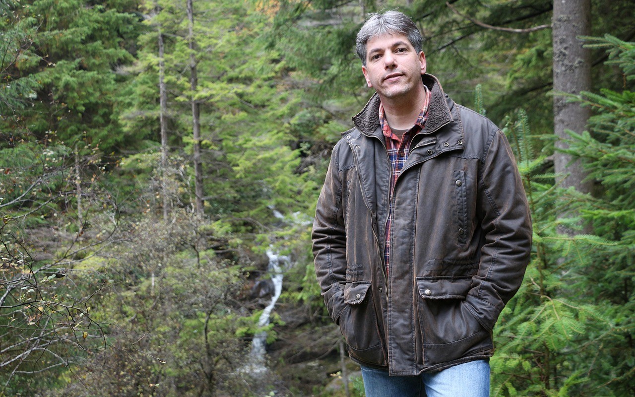 Ein Mann steht in einem Wald mit Wasserfall – eine Szene, die den Schutz von Wäldern und natürlichen Ökosystemen gemäß SDG 15 hervorhebt.