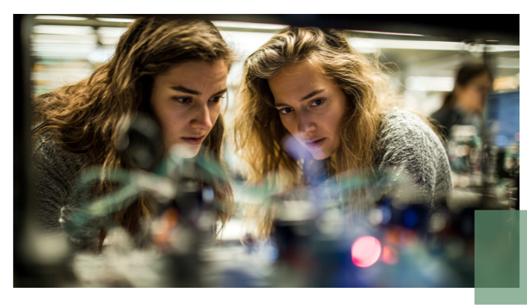 Zwei Frauen blicken konzentriert auf ein technisches Gerät mit vielen Kabeln und Lichtern.