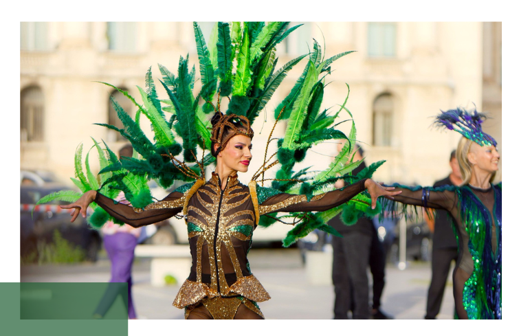 A dancer in an elaborate green feather costume performs outdoors during a cultural event. The scene illustrates the importance of cultural diversity and vibrant public spaces.