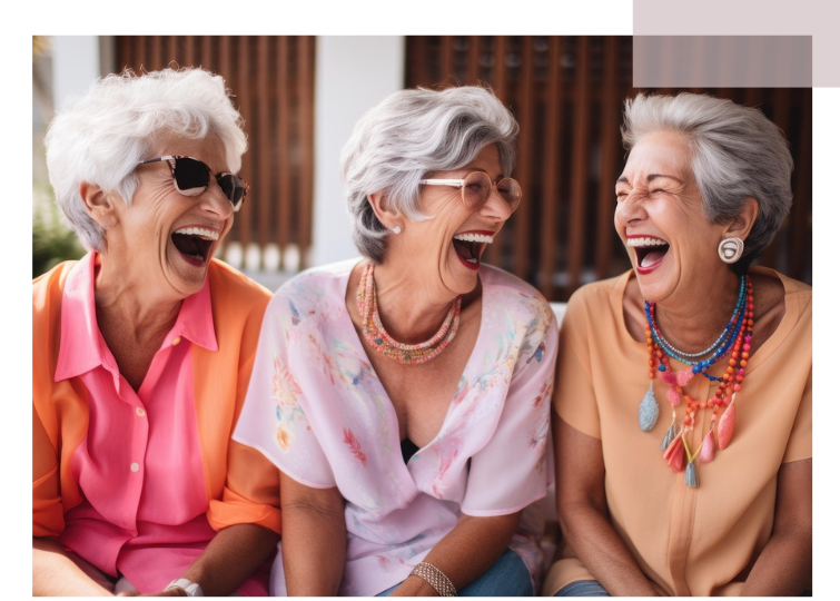 Three elderly women sitting side by side, wearing colorful tops and multiple beaded necklaces.