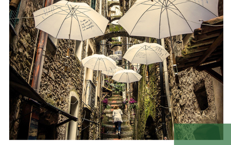 A narrow, stone, old town alley with steps is decorated with hanging white umbrellas. A person walks up the stairs. The scene stands for creative, livable urban design and the protection of historic city structures.